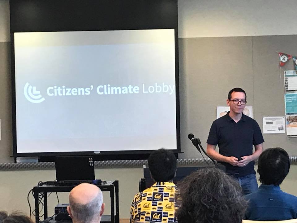 Photo of a man facing an audience with a slideshow slide that says Citizens' Climate Lobby