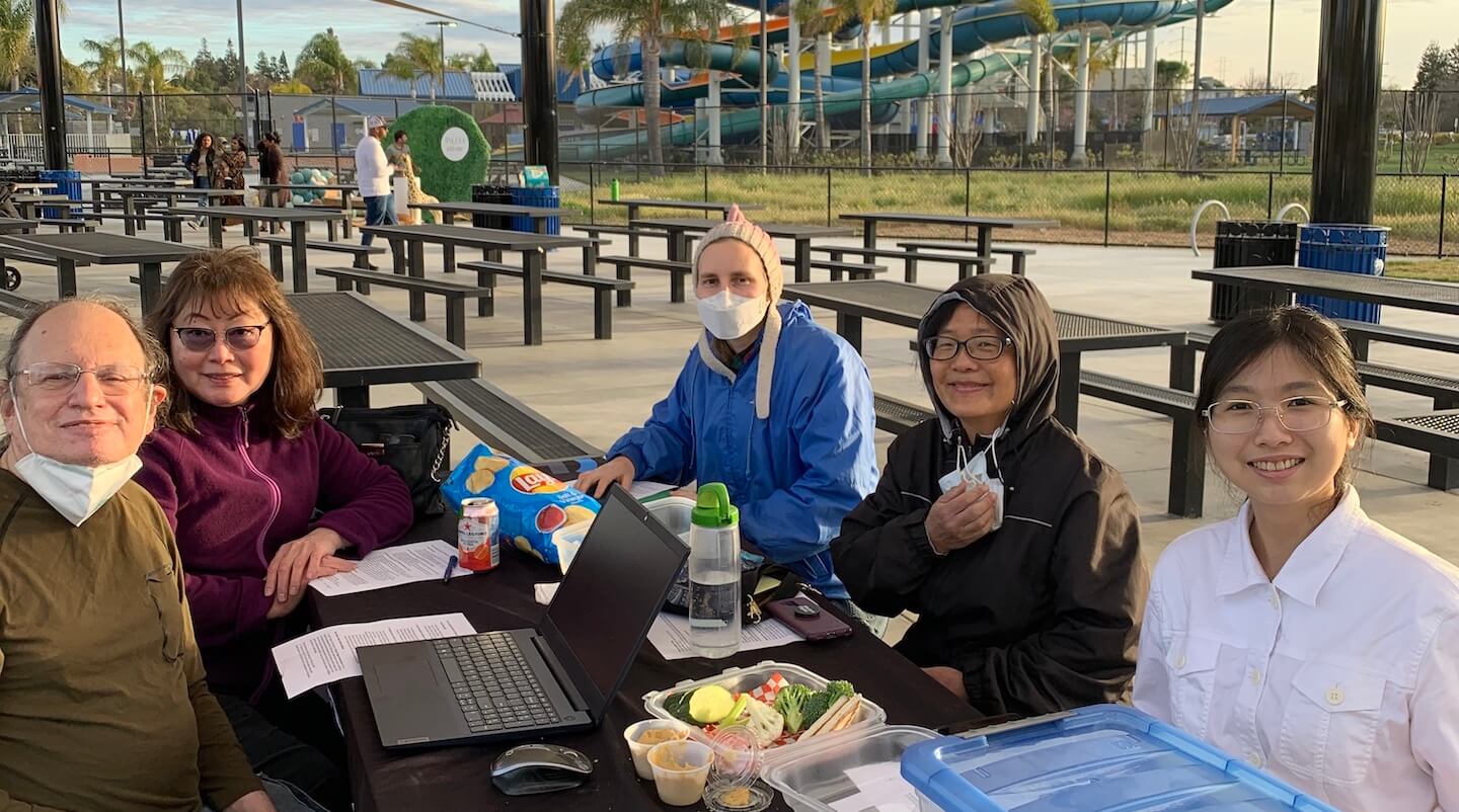 Photo of five people sitting around a table at a park